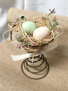 three eggs are in a nest on a stand with flowers and twine around it