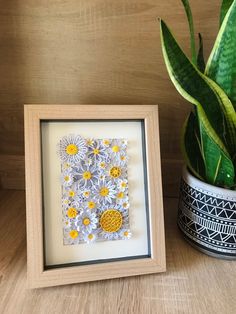 a vase with some flowers in it next to a framed piece of paper and a potted plant