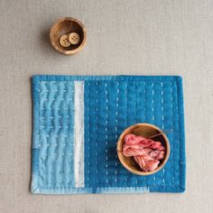 a bowl with yarn in it sitting on top of a blue mat next to a wooden bowl