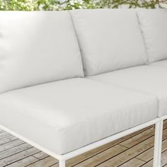 a white couch sitting on top of a wooden floor next to a wall with trees in the background