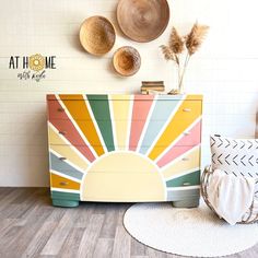 a dresser with sun painted on it next to some pillows and hats hanging on the wall