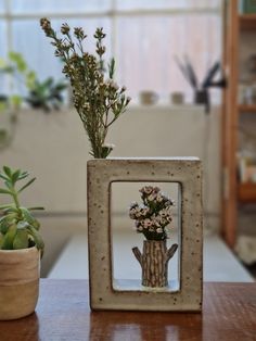 there are two small vases with flowers in them on the table next to each other