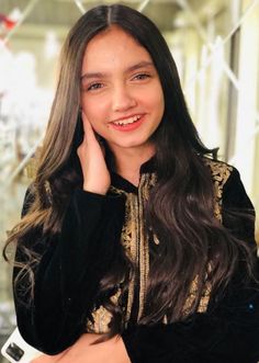 a young woman with long hair wearing a black and gold dress smiling at the camera