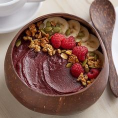 a bowl filled with fruit and nuts on top of a wooden table next to a spoon