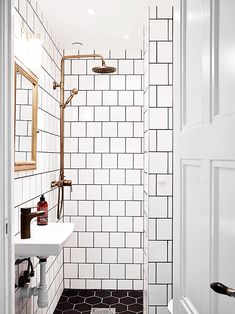 a white bathroom with black and white tile on the floor, shower head, sink and mirror