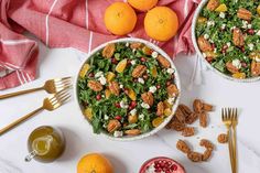 two bowls filled with salad next to oranges and other food on a white table