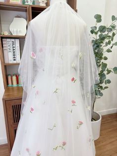 the back of a wedding dress with flowers on it and a white veil over it