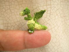 a tiny crocheted green dragon sitting on top of a persons finger