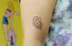 a woman's arm with a small leaf tattoo on it