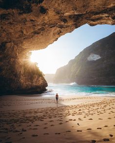 a person walking on the beach in front of an ocean cave with sunlight coming through