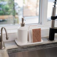 a soap dispenser, sponge and kitchen sink faucet in front of a window