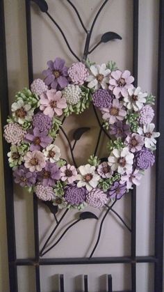 a wreath with purple flowers hanging on a metal wall mounted in front of a door