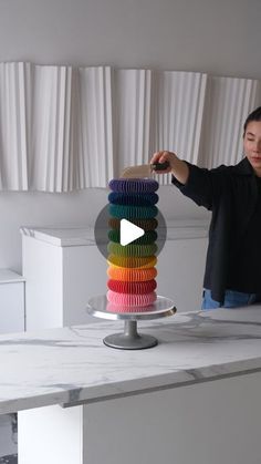 a man standing in front of a cake on top of a table with stacks of colorful cupcakes