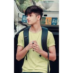 a young man standing in front of a parked car with his hands clasped to his chest