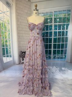 This handmade gown features an elegant lavender base adorned with vintage-inspired floral prints, exuding a sense of romantic charm. The delicate spaghetti straps and ruched bodice accentuate the feminine silhouette, while the tiered ruffle details on the skirt add a touch of playful movement. Perfect for outdoor weddings, evening events, or special occasions, this gown is sure to make you the center of attention. The lace-up back not only enhances the vintage appeal but also allows for a custom Spaghetti Strap Gown, Purple Floral Dress, Lavender Floral, Outdoor Weddings, Ruched Bodice, Feminine Silhouette, Floral Ruffle, Tiered Dress, Corset Dress