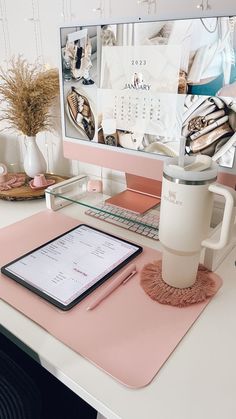 a desk with a tablet, coffee mug and pen on it next to a desktop computer