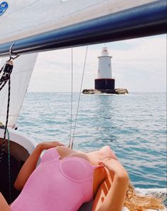 a woman laying on top of a boat in the ocean next to a light house