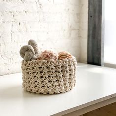 two balls of yarn sit in a basket on a white table next to a brick wall