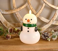 a frosty snowman sitting on top of a wooden table next to pine cones