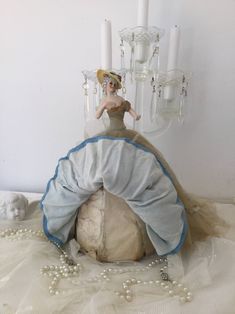 a figurine sitting on top of a ball with pearls around it and candles in the background