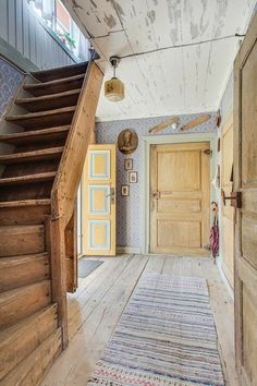 an old wooden staircase leads up to a bright yellow door in this rustic home with blue and white wallpaper