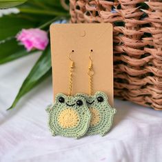 two crocheted frog earrings sitting next to each other