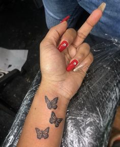 a woman's hand with three butterflies tattooed on her left wrist and red nail polish