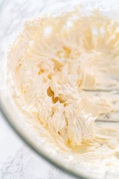 a close up of a frosted cake in a glass bowl on a white table