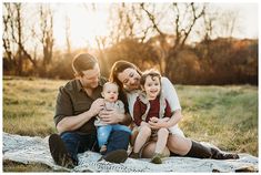 a family sitting on a blanket in the middle of a field with trees behind them