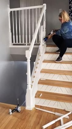 a woman kneeling down on the stairs in front of a stair case and paint rollers