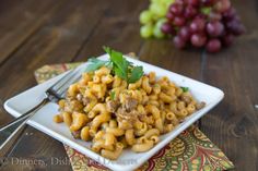 a white plate topped with pasta and meat on top of a table next to grapes