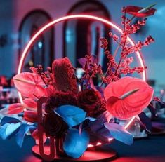 an arrangement of flowers and foliage in a vase on a table with red lights behind it