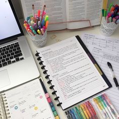 an open laptop computer sitting on top of a desk next to notebooks and pens