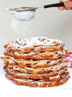 a person is sprinkling sugar on a stack of churros