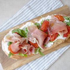 a sandwich with meat, tomatoes and lettuce on a cutting board next to a towel