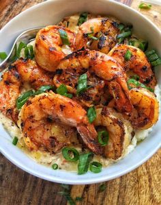 a white bowl filled with shrimp and grits on top of a wooden table next to a fork