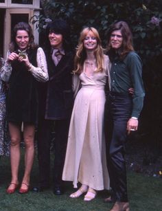 three women and one man are posing for a photo in front of a house with flowers