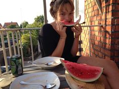 a woman sitting at a table eating a slice of watermelon