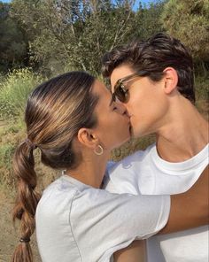 a man and woman kissing each other in front of some brushy hills with trees