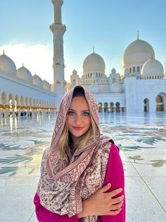 a woman standing in front of a white building wearing a pink dress and a shawl