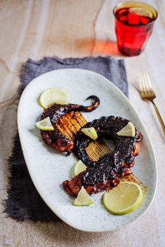 a white plate topped with grilled meat and lemon wedges