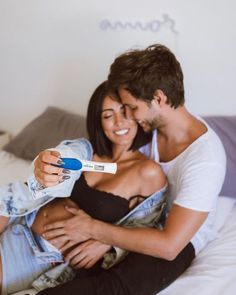 a man and woman sitting on a bed holding a thermometer in their hands