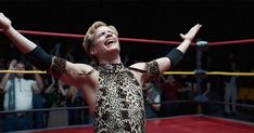 a woman with her arms up in the air while standing next to a wrestling ring