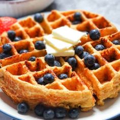 waffles with blueberries and butter are on a plate next to strawberries