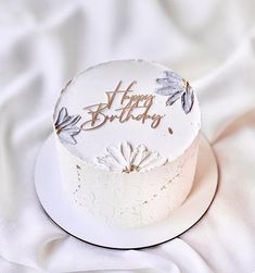 a white birthday cake sitting on top of a white cloth covered tablecloth with the words happy birthday written on it