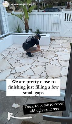 a man kneeling down on top of a cement floor next to a white fence and potted plant