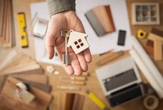 a person holding a house key in their hand with lots of other items on the table