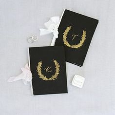 two black wedding guest book with gold monogrammed wreaths and initials on them