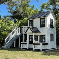 a white house with black shutters and a slide in the front yard, surrounded by trees