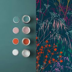 four paint cans with different colors on them next to a wallpapered plant pattern